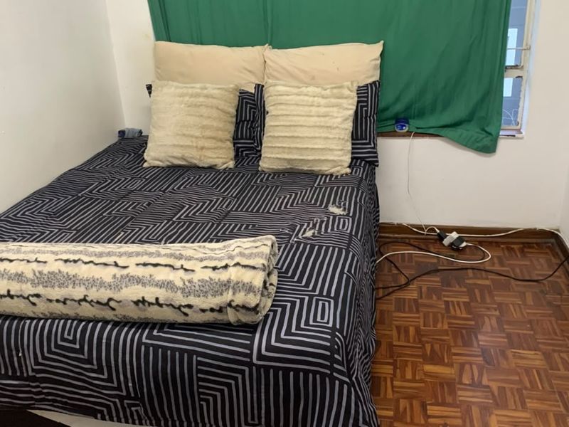 A compact bedroom featuring traditional parquet flooring and a window, offering a functional space that would benefit from cosmetic updates and modern finishes.