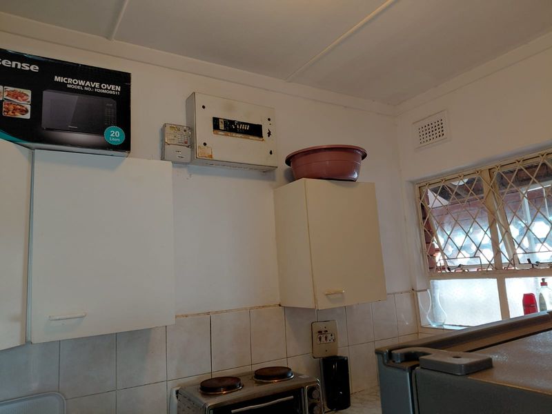 A functional kitchen area featuring wall-mounted cabinetry, a tiled splashback, and an integrated electrical distribution board with security burglar bars on the window.