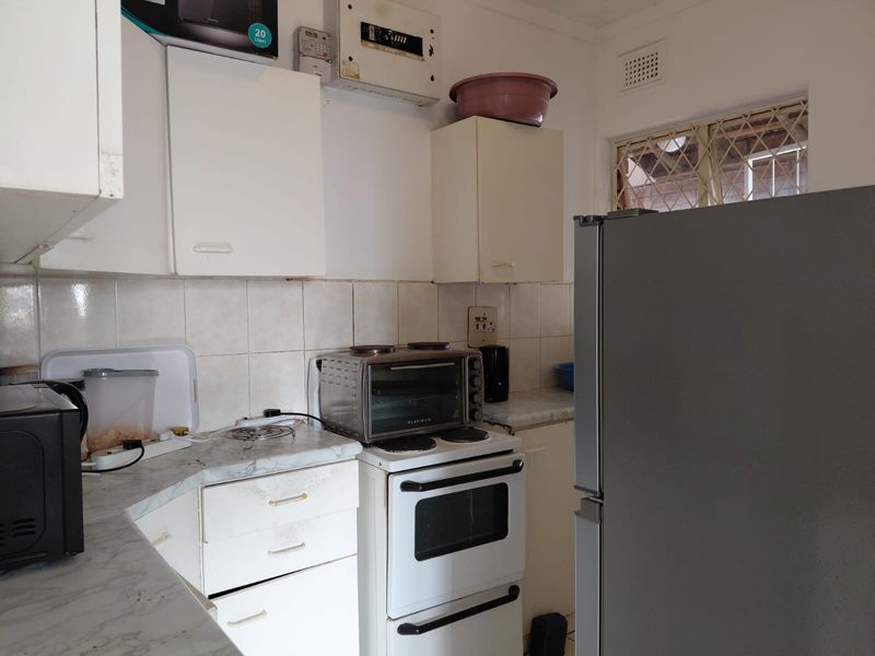 A compact kitchen featuring dated cabinetry, a tiled backsplash, laminate countertops, and a freestanding stove, requiring cosmetic updates to modernize the space.