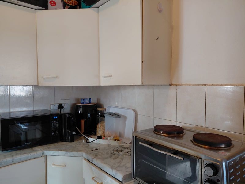A compact kitchen area featuring white cabinetry, laminate countertops, and a tiled backsplash, showing signs of wear and dated finishes.