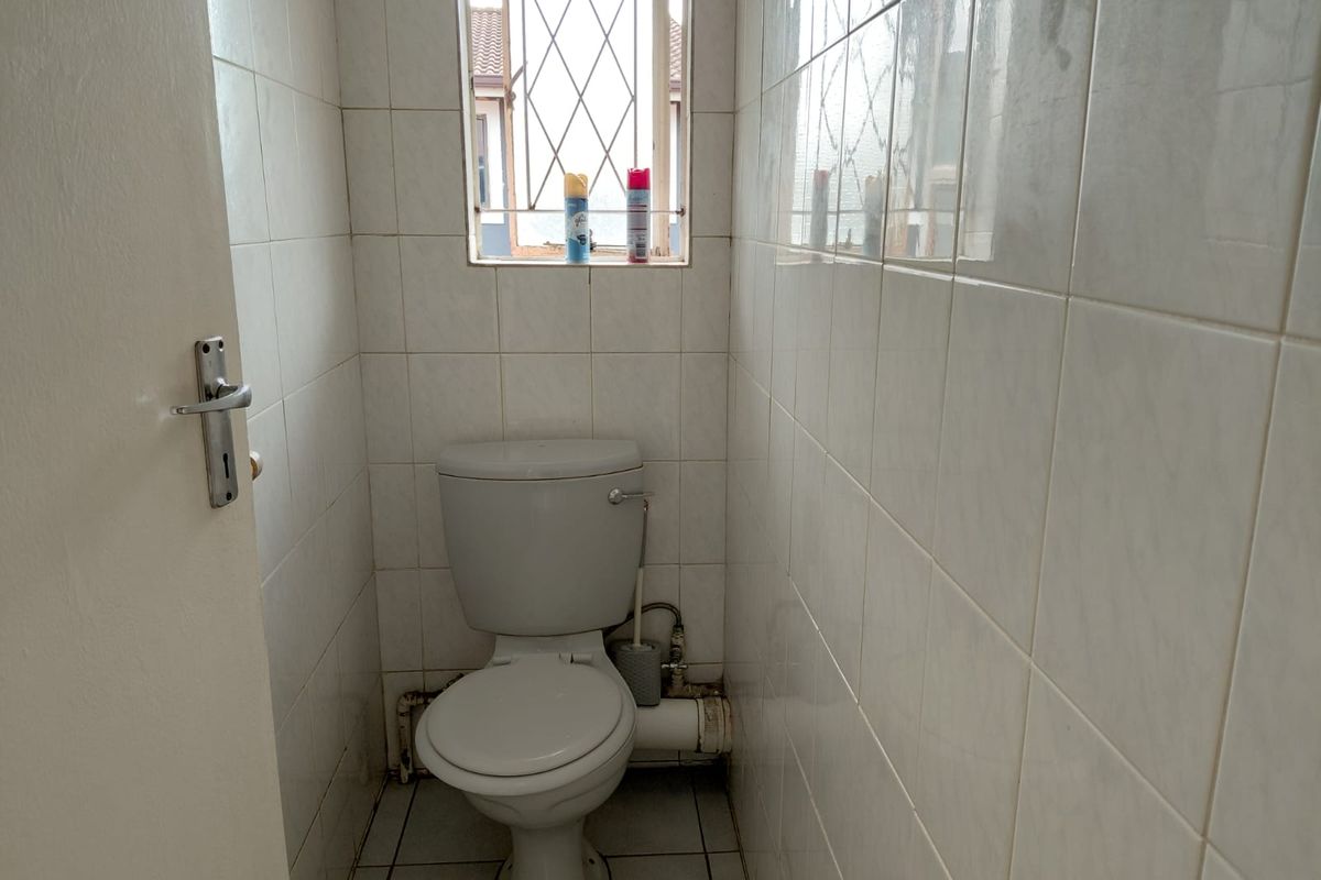 A compact, tiled guest toilet featuring a standard white toilet suite and a small window with security bars.