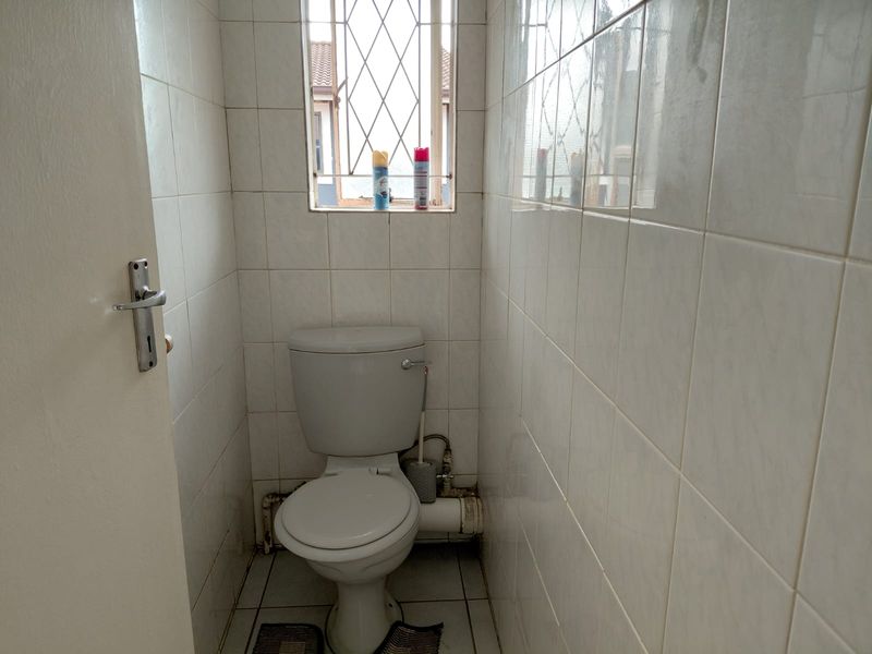 A compact, tiled guest toilet featuring a standard white toilet suite and a small window with security bars.