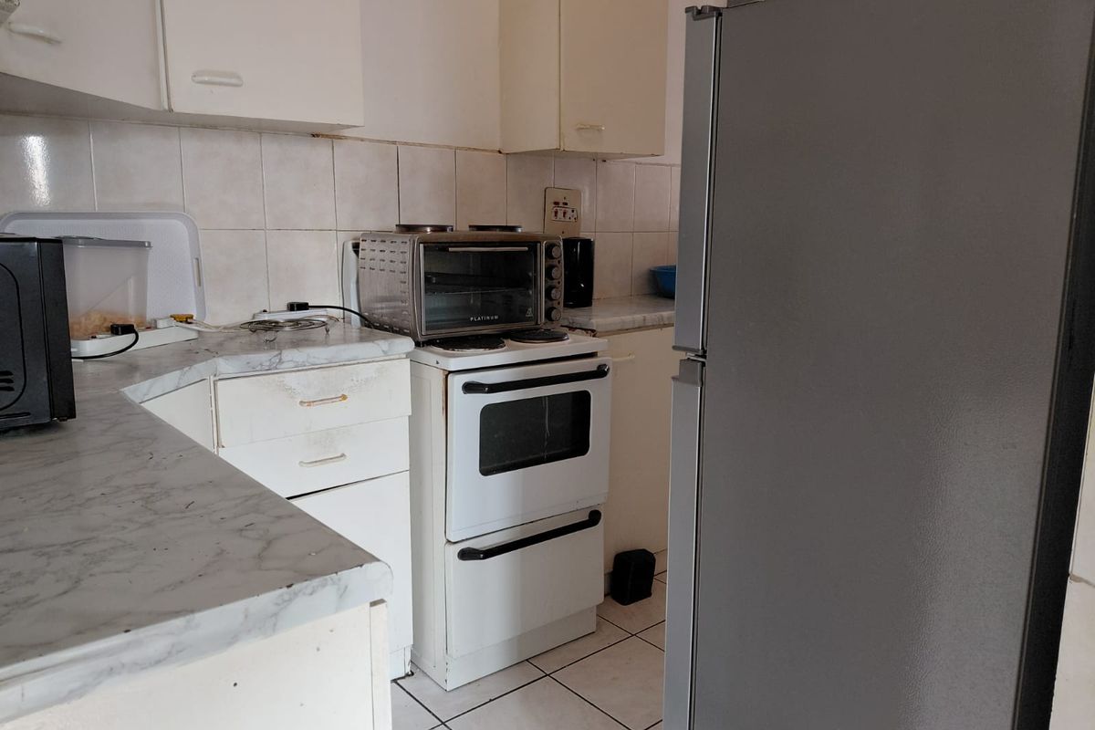 A compact kitchen featuring dated cabinetry, laminate countertops, and a tiled backsplash, offering potential for a modern renovation to enhance functionality and aesthetic appeal.