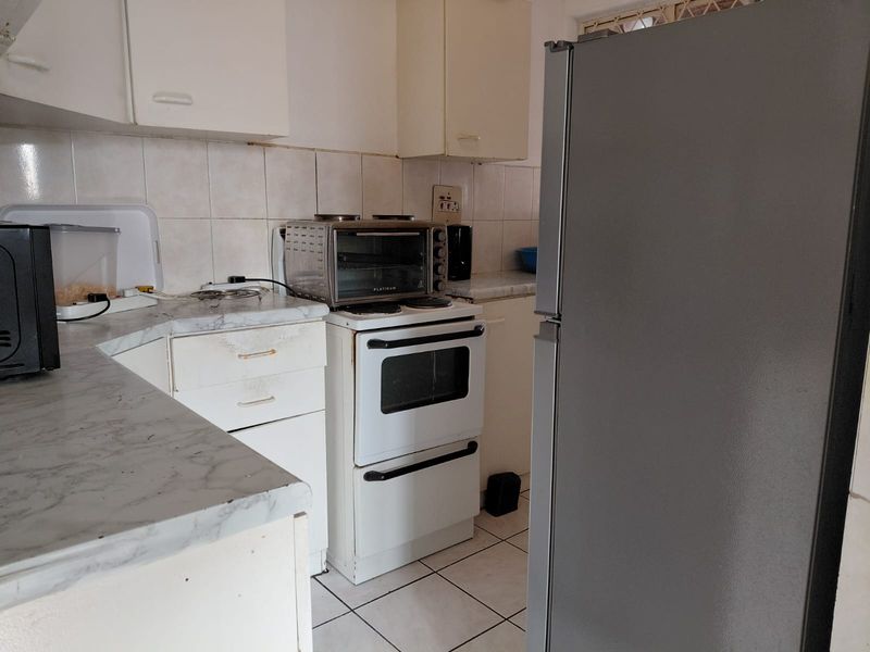 A compact kitchen featuring dated cabinetry, laminate countertops, and a tiled backsplash, offering potential for a modern renovation to enhance functionality and aesthetic appeal.