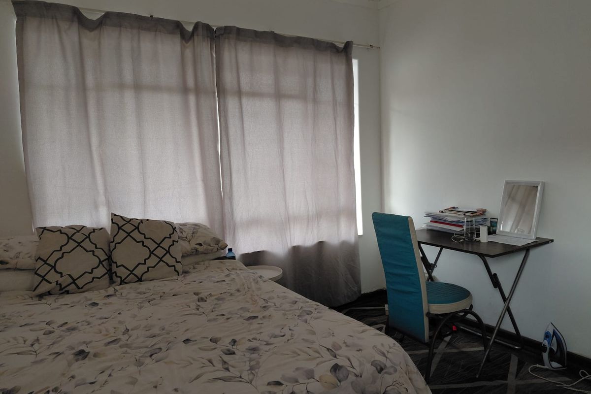 A functional bedroom featuring a large window with curtains and neutral wall finishes, providing a comfortable and well-lit sleeping space.
