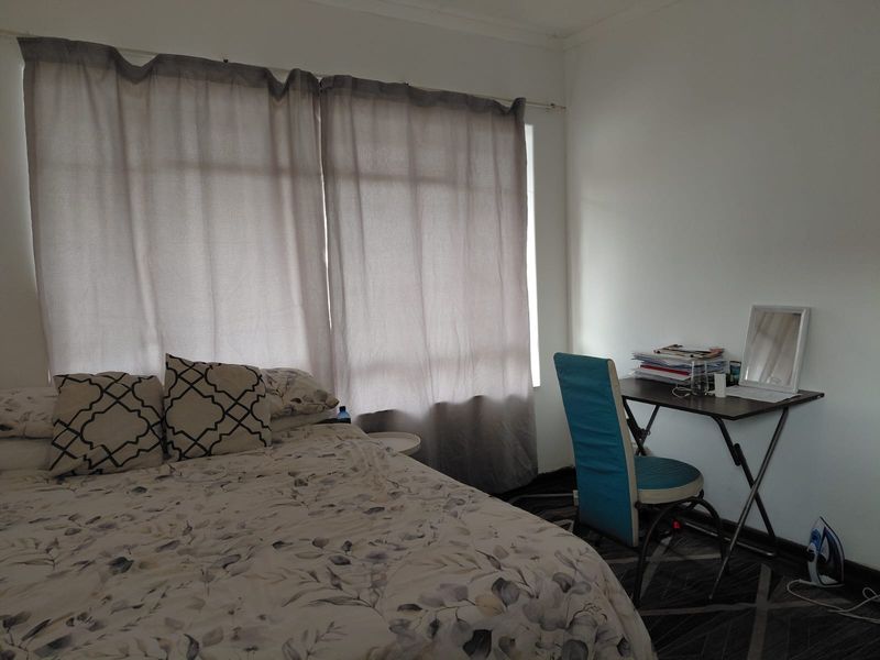 A functional bedroom featuring a large window with curtains and neutral wall finishes, providing a comfortable and well-lit sleeping space.