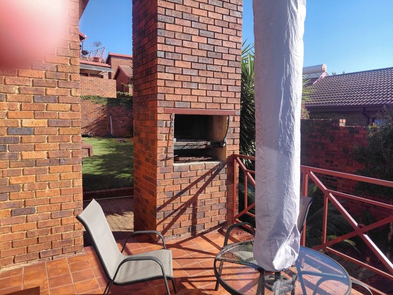 Covered patio area featuring a built-in brick braai, tiled flooring, and direct access to the rear garden space.