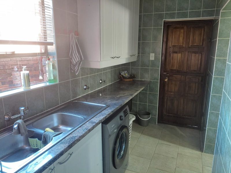 Functional laundry room featuring built-in cabinetry, a stainless steel sink, laminate countertops, and tiled finishes throughout.
