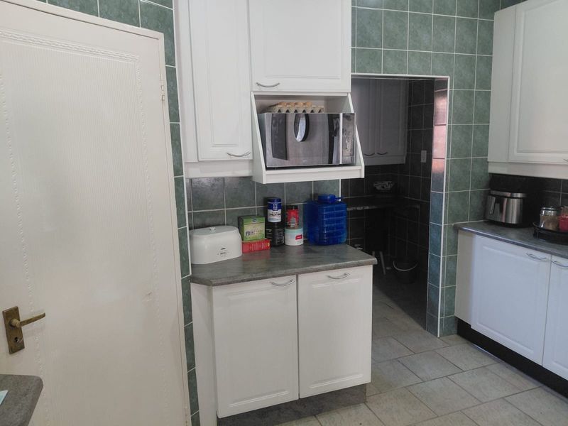 A functional kitchen featuring white cabinetry, tiled backsplash, and laminate countertops, with an adjacent scullery area visible through the doorway.