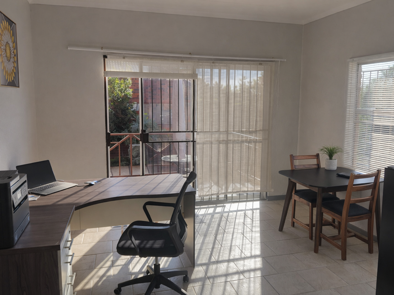 A functional home office space featuring tiled flooring, vertical blinds on the sliding door, and natural light, with direct access to an outdoor area.