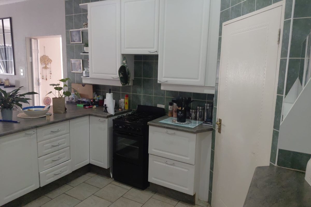 A functional kitchen featuring white cabinetry, dark laminate countertops, a freestanding stove, and green ceramic wall tiling.