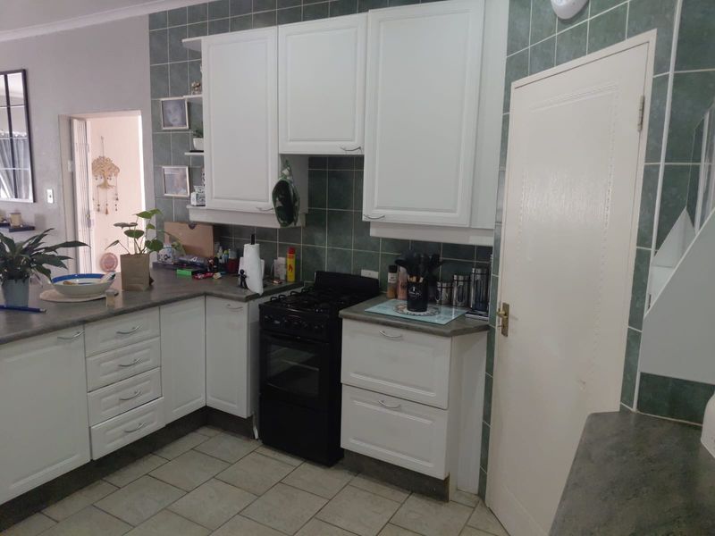 A functional kitchen featuring white cabinetry, dark laminate countertops, a freestanding stove, and green ceramic wall tiling.