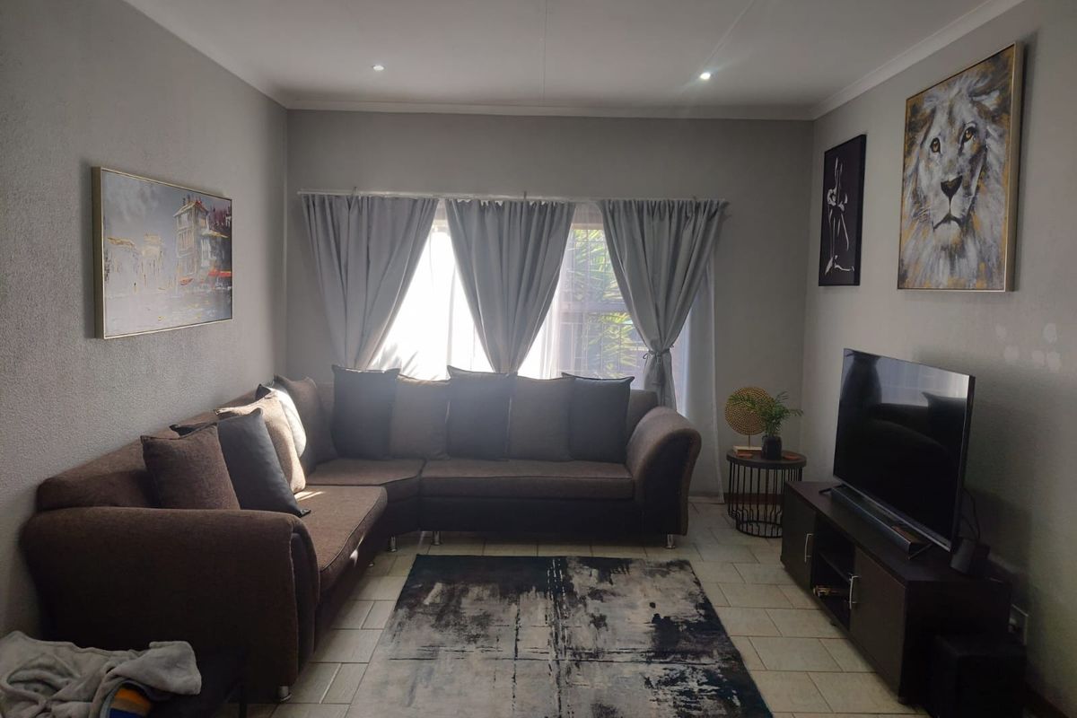 A comfortable living room featuring tiled flooring, recessed downlighting, and large windows with curtain rails, creating a functional and well-lit space.