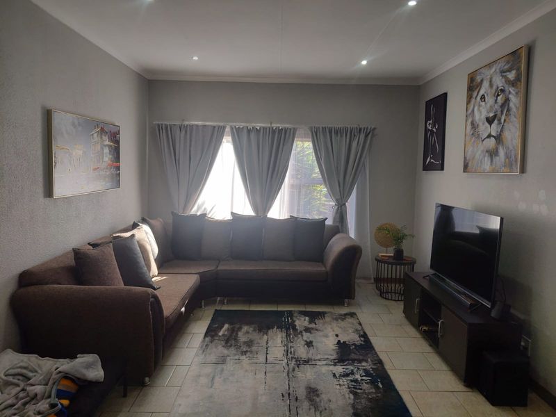A comfortable living room featuring tiled flooring, recessed downlighting, and large windows with curtain rails, creating a functional and well-lit space.