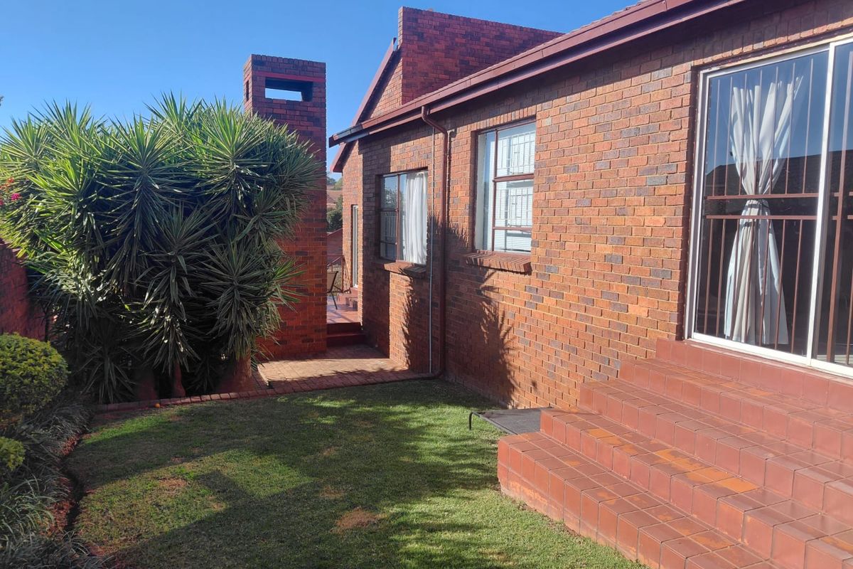 Rear view of a face brick cluster home featuring a paved walkway, tiled entrance steps, and a brick chimney structure.