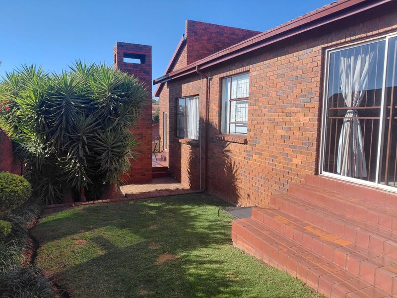 Rear view of a face brick cluster home featuring a paved walkway, tiled entrance steps, and a brick chimney structure.