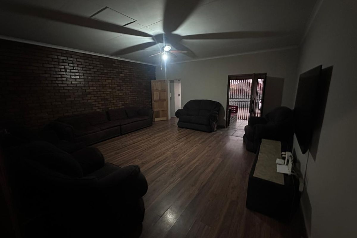 Spacious living room featuring an exposed brick accent wall, laminate flooring, and a ceiling fan, with direct access to an outdoor area.