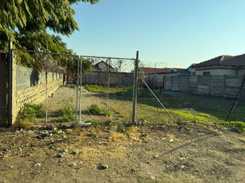 Vacant residential land plot featuring perimeter chain-link fencing, a metal gate, and precast concrete boundary walls, requiring site clearance and maintenance.