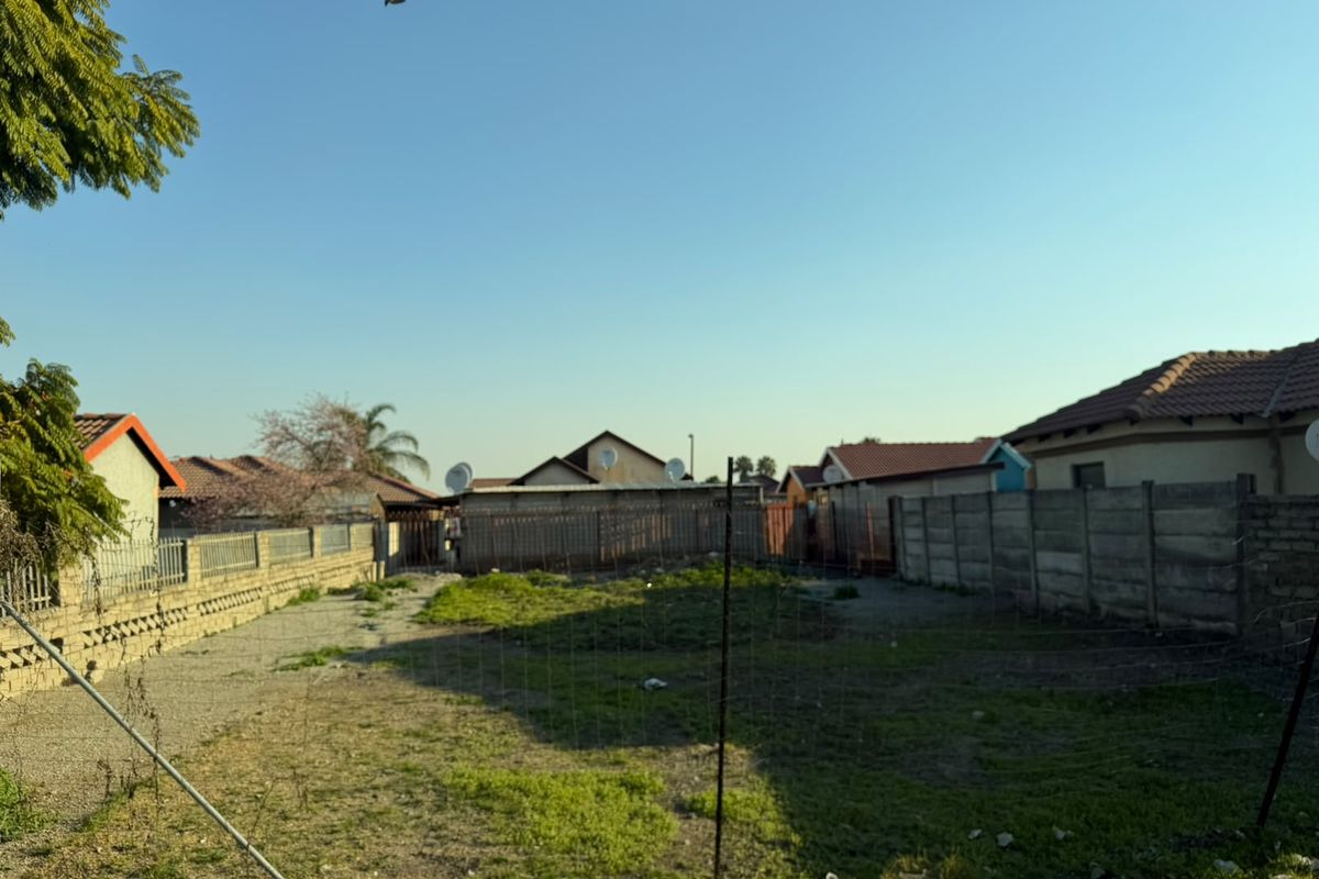 A vacant residential plot enclosed by precast concrete boundary walls and wire fencing, featuring an open grassed area.