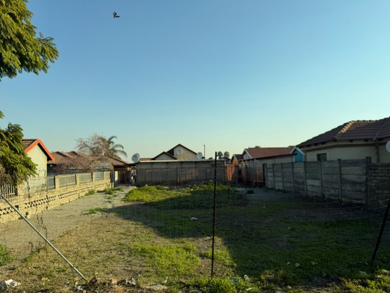 A vacant residential plot enclosed by precast concrete boundary walls and wire fencing, featuring an open grassed area.