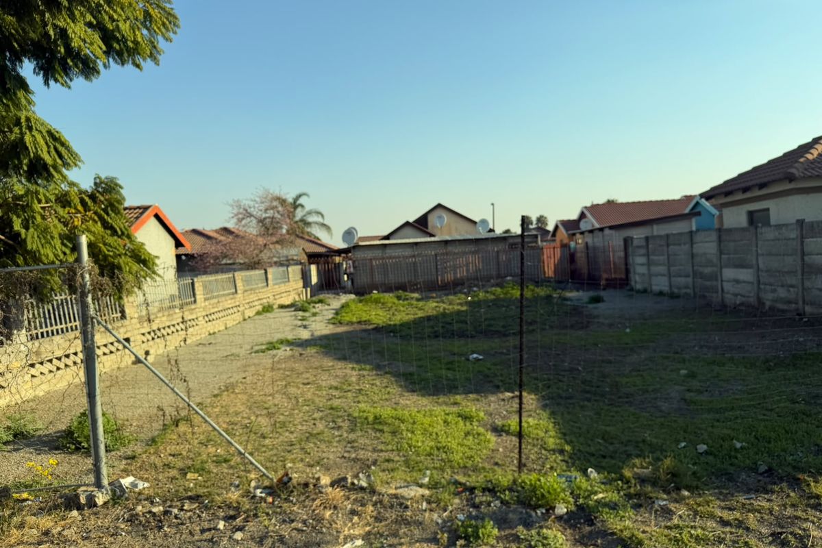 A vacant residential plot enclosed by precast concrete boundary walls and wire mesh fencing, offering a clear space for potential development.