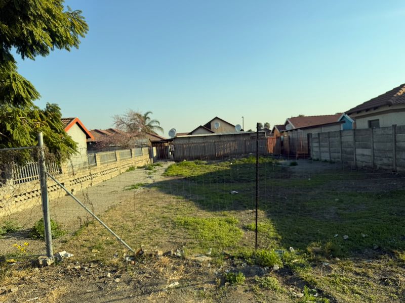 A vacant residential plot enclosed by precast concrete boundary walls and wire mesh fencing, offering a clear space for potential development.
