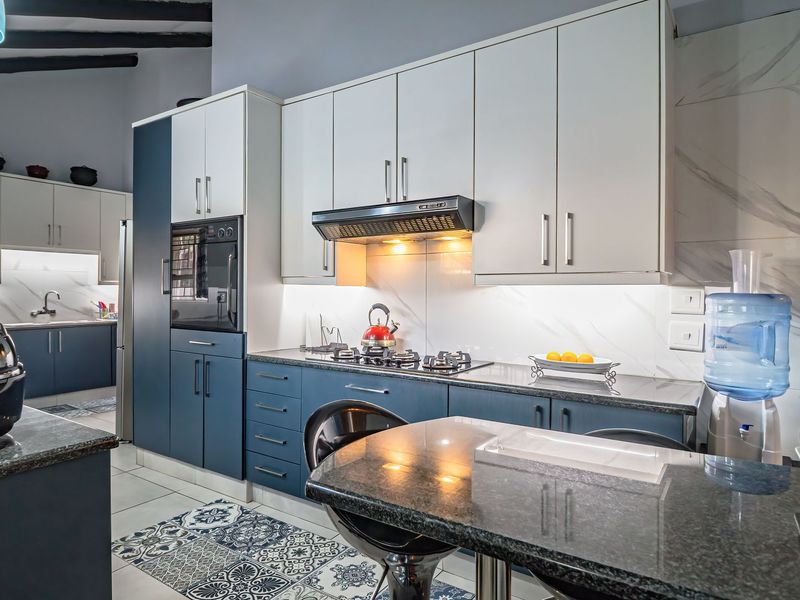 Modern kitchen featuring two-tone cabinetry, stone countertops, gas hob with extractor, built-in oven, and stylish tiled flooring with exposed ceiling beams.