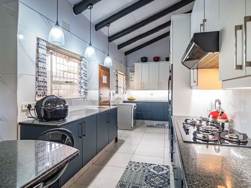 Modern kitchen featuring granite countertops, gas hob, extractor fan, built-in oven, and stylish pendant lighting under exposed ceiling beams.