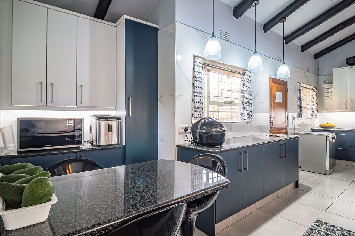 Modern kitchen featuring dark blue and white cabinetry, granite countertops, tiled backsplash, and exposed ceiling beams with contemporary pendant lighting.