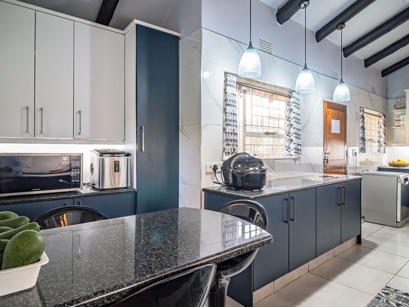 Modern kitchen featuring dark blue and white cabinetry, granite countertops, tiled backsplash, and exposed ceiling beams with contemporary pendant lighting.