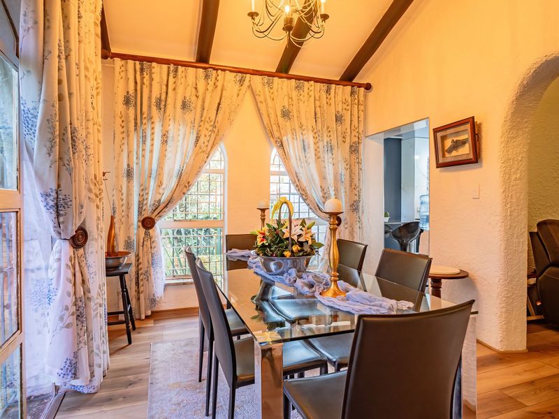A bright dining room featuring exposed timber ceiling beams, laminate flooring, and an arched doorway leading to adjacent living spaces.