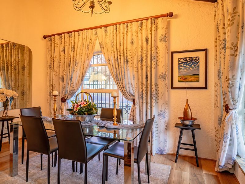 A well-maintained dining room featuring hardwood flooring, an arched window with security bars, and a large wall mirror, creating a bright and inviting space.