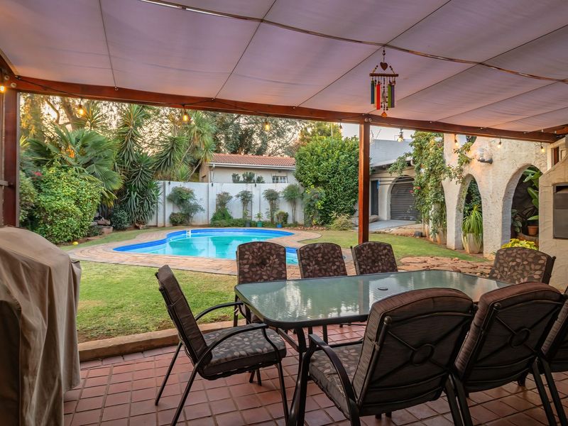 Covered outdoor patio featuring a built-in braai, overlooking a private garden and swimming pool area, ideal for outdoor entertaining.