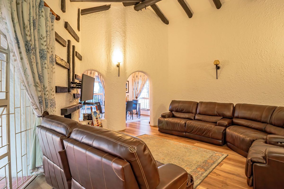 Spacious living room featuring high ceilings with exposed timber beams, textured walls, arched architectural details, and laminate flooring with access to an outdoor area.