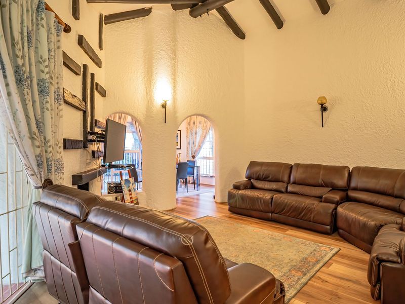 Spacious living room featuring high ceilings with exposed timber beams, textured walls, arched architectural details, and laminate flooring with access to an outdoor area.