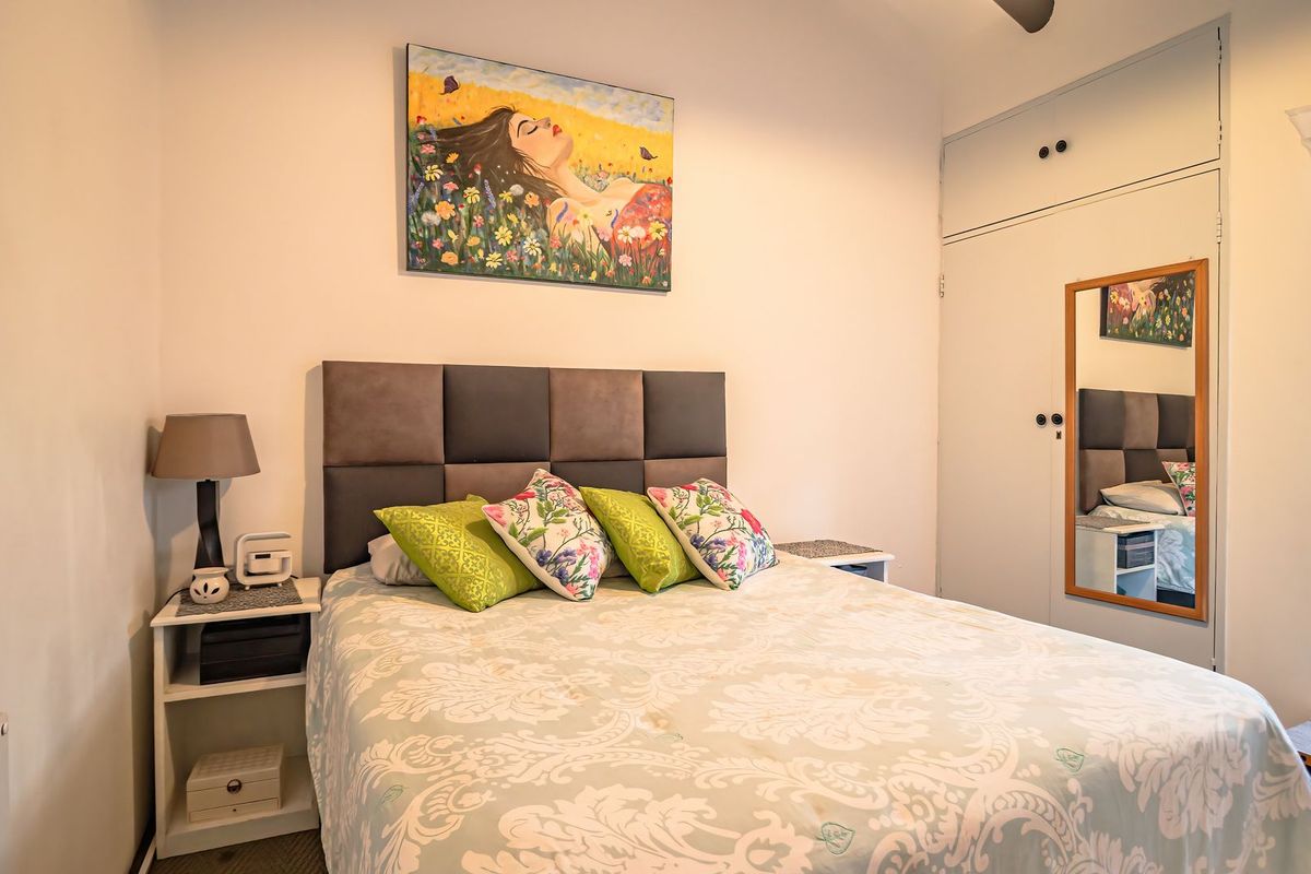 A cozy bedroom featuring built-in cupboards, a ceiling fan, and a window with security bars, providing a functional and comfortable living space.