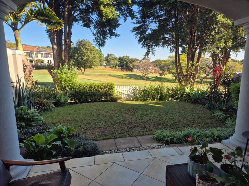 A covered patio featuring tiled flooring and columns, overlooking a private landscaped garden with views of the surrounding estate grounds.