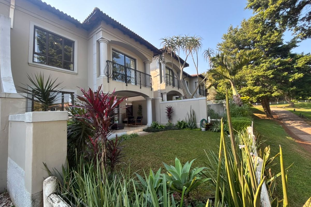Rear view of a townhouse featuring a landscaped garden, covered patio, and upper-level balconies with wrought iron railings.