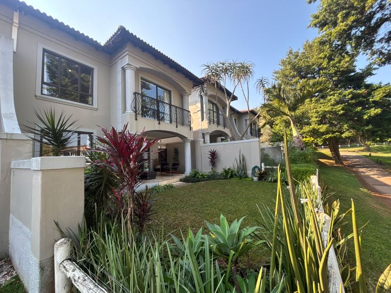 Rear view of a townhouse featuring a landscaped garden, covered patio, and upper-level balconies with wrought iron railings.