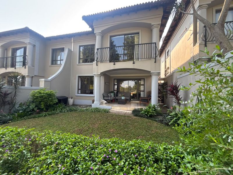 Rear view of a townhouse featuring a covered patio, an upper-level balcony with wrought iron railings, and a well-maintained private garden.