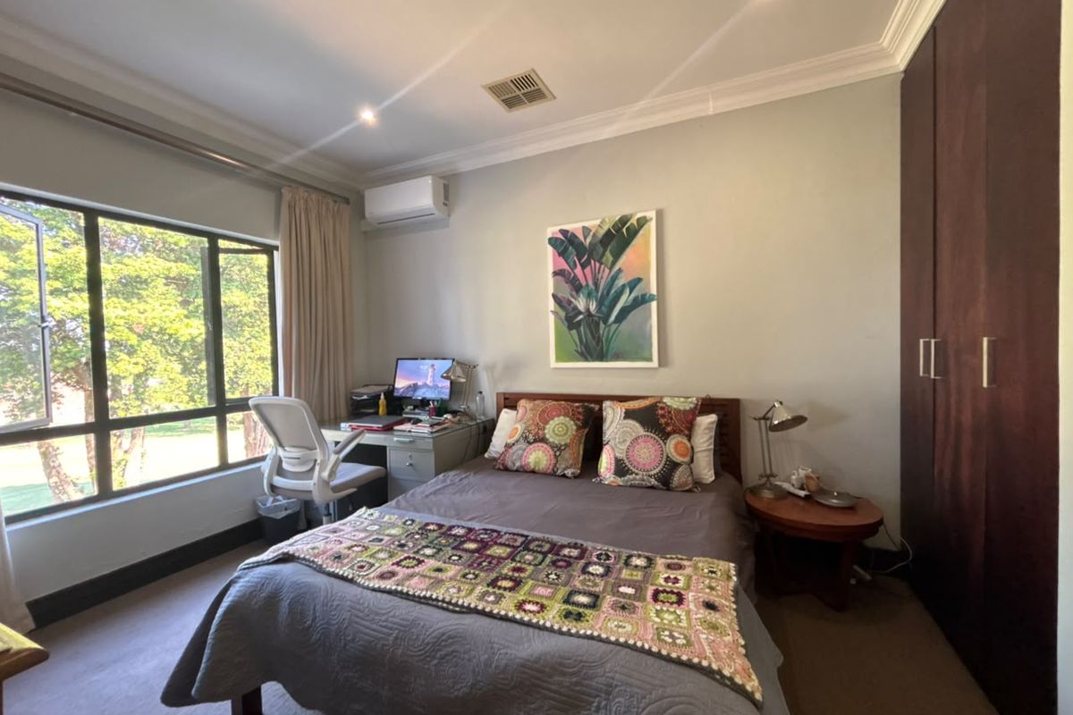 A well-maintained bedroom featuring built-in cupboards, an air conditioning unit, and large windows providing natural light and garden views.