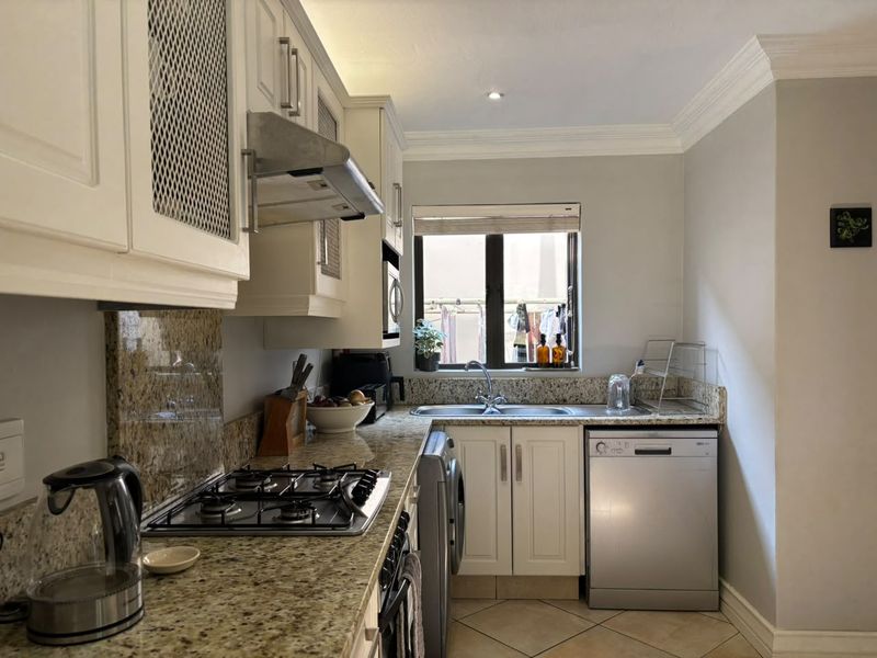 A functional kitchen featuring granite countertops, a gas hob with extractor fan, built-in cabinetry, and tiled flooring, offering a practical workspace.