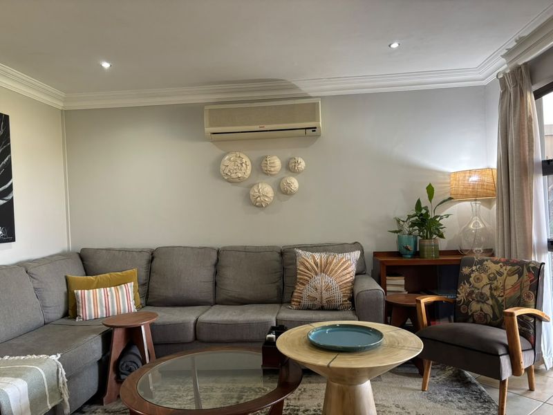 A comfortable living room featuring crown molding, recessed downlighting, and a wall-mounted split-system air conditioning unit.