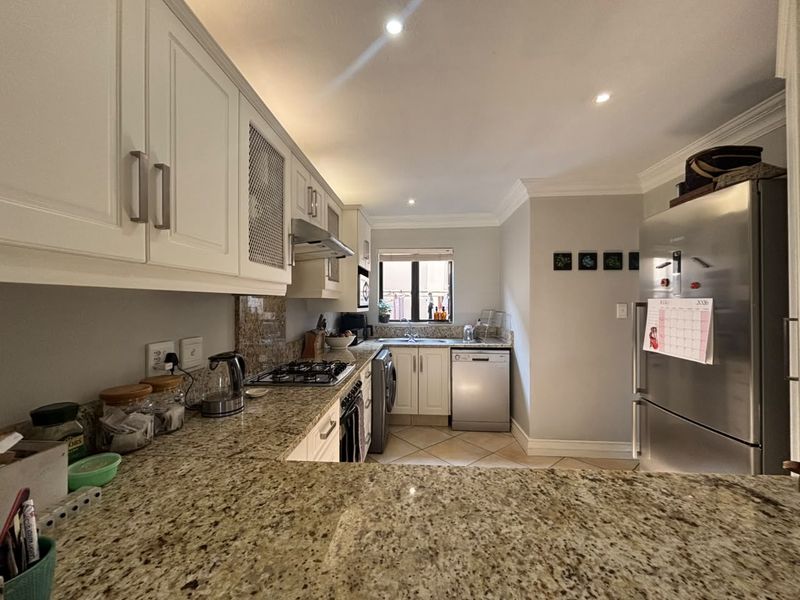 A well-maintained kitchen featuring granite countertops, white cabinetry, a gas hob, and integrated appliances, offering a functional and clean workspace.