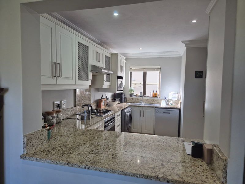A functional kitchen featuring granite countertops, white cabinetry, a gas hob, and integrated appliances, offering a clean and practical workspace.
