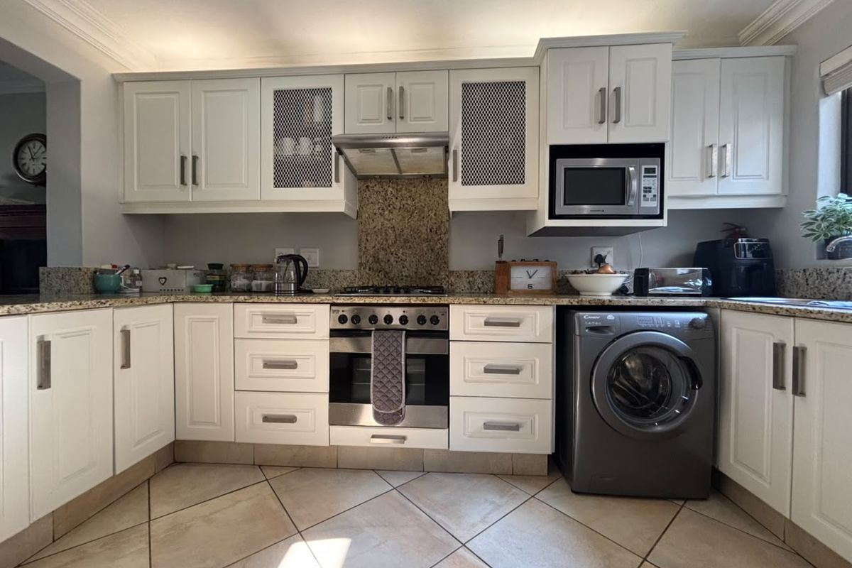 A well-maintained kitchen featuring white cabinetry, granite countertops, built-in oven with gas hob, extractor fan, and integrated microwave.