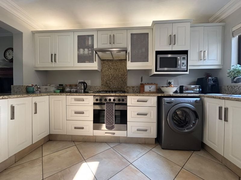A well-maintained kitchen featuring white cabinetry, granite countertops, built-in oven with gas hob, extractor fan, and integrated microwave.