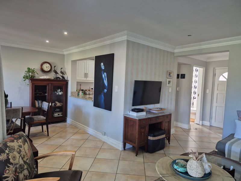 Open-plan living area featuring ceramic floor tiles, crown molding, and a convenient pass-through window connecting to the kitchen space.