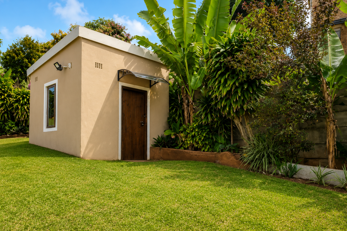 A well-maintained detached outbuilding or studio space situated in a lush, landscaped garden setting with a manicured lawn.