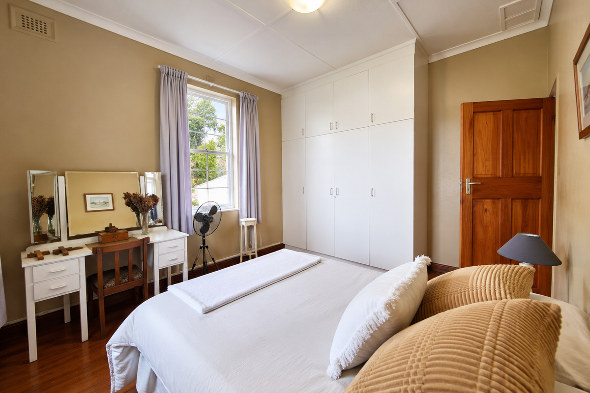 A well-maintained bedroom featuring timber flooring, a large built-in wardrobe, and a classic timber door, offering a comfortable and functional living space.